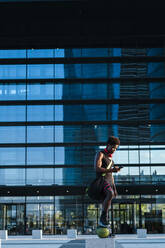 Junger Mann mit Basketball und Smartphone in einem modernen Gebäude in der Stadt - JMPF00059