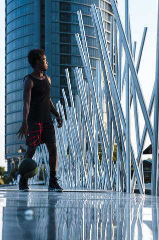 Junger Mann spielt Basketball in moderner Stadtumgebung, lizenzfreies Stockfoto