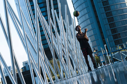 Young man playing basketball in modern city surrounding - JMPF00063