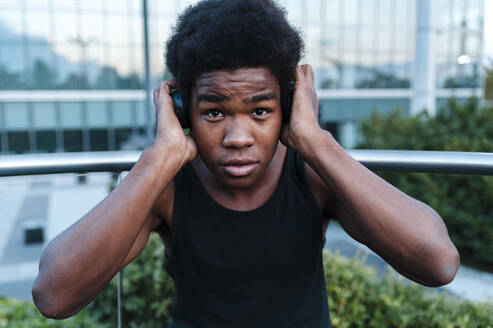 Porträt eines jungen Mannes mit Kopfhörern beim Musikhören in der Stadt - JMPF00064