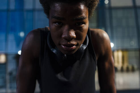 Portrait of a young athletic man with headphones at dusk in city - JMPF00066