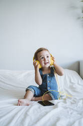 Baby girl at home listening to music on bed - EBBF00323