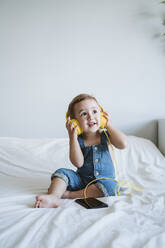 Kleines Mädchen zu Hause beim Musikhören im Bett - EBBF00323