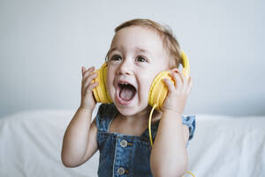 Baby girl at home listening to music on bed - EBBF00325