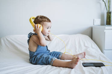 Baby girl at home listening to music on bed - EBBF00326