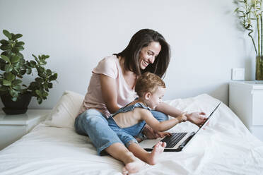 Mother and baby girl using laptop on bed at home - EBBF00334