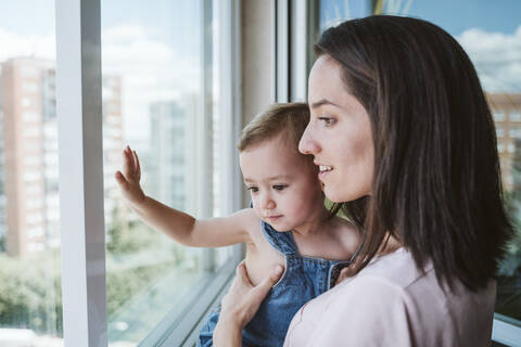 Mutter mit kleinem Mädchen zu Hause am Fenster, lizenzfreies Stockfoto