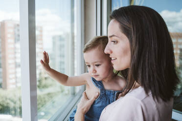 Mother with baby girl at home looking by the window - EBBF00352