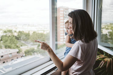 Mother with baby girl at home looking by the window - EBBF00354