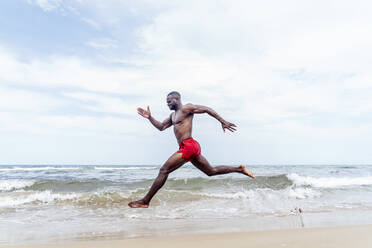 Sportlicher Mann läuft am Strand - OCMF01401