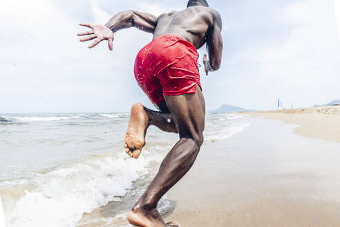 Rear view of athletic man running on beach - OCMF01411