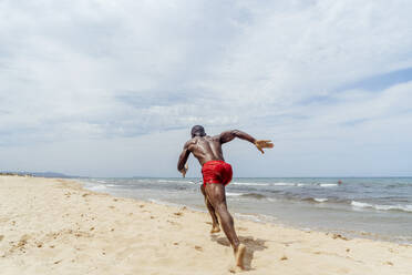 Rückansicht eines sportlichen Mannes, der am Strand läuft - OCMF01412