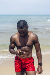 Sportlicher Mann mit Smartphone am Strand - OCMF01414