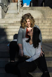 Lesbisches Paar sieht sich an, während es auf einer Treppe in der Stadt sitzt - JMPF00071