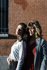 Lesbian couple with eyes closed standing against brick wall during sunny day - JMPF00074