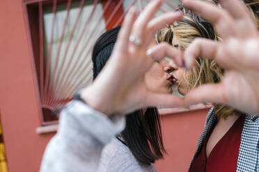 Close-up of lesbian couple making heart shape with hands while kissing in city - JMPF00079