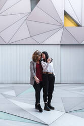 Romantisches lesbisches Paar auf dem Fußweg vor einem modernen Gebäude in der Stadt - JMPF00089