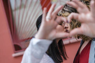 Close-up of lesbian couple gesturing heart shape with hands while kissing in city - JMPF00094