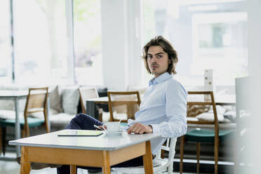 Serious businessman with coffee on table sitting in cafe - KNSF08106