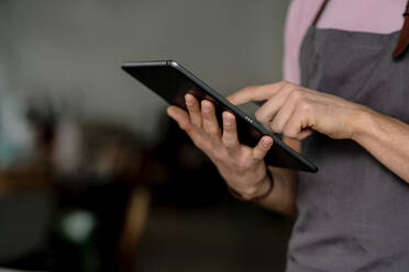 Nahaufnahme eines männlichen Besitzers, der ein digitales Tablet benutzt, während er in einem Cafe steht - KNSF08107