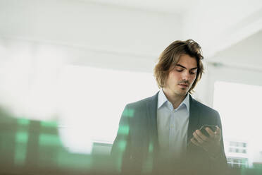 Male entrepreneur using smart phone while standing in restaurant - KNSF08128