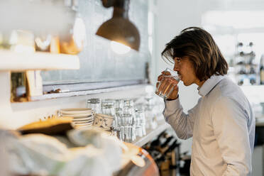 Businessman drinking water while standing in cafe - KNSF08143