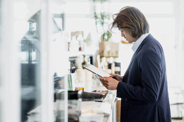 Businessman using digital tablet while standing at counter in cafe - KNSF08144