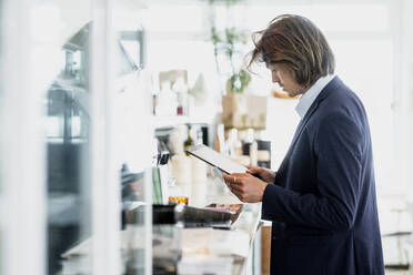 Geschäftsmann, der ein digitales Tablet benutzt, während er am Tresen eines Cafés steht - KNSF08144