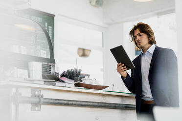 Male entrepreneur using digital tablet while standing in coffee shop - KNSF08147