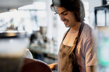 Smiling male owner working while standing in coffee shop - KNSF08154