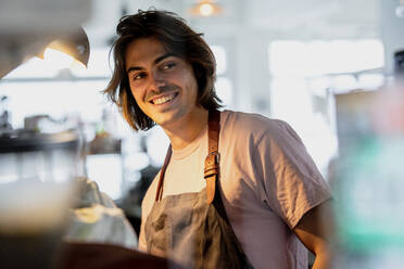 Lächelnder männlicher Besitzer, der bei der Arbeit in einem Café wegschaut - KNSF08155