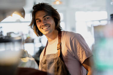 Smiling male owner looking away while working in coffee shop - KNSF08155