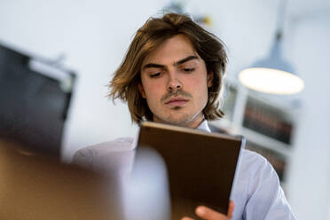 Nahaufnahme eines männlichen Berufstätigen, der ein digitales Tablet benutzt, während er in einem Café sitzt - KNSF08175