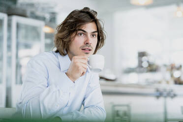 Nachdenklicher männlicher Berufstätiger, der in einem Café sitzt und Kaffee trinkt - KNSF08183