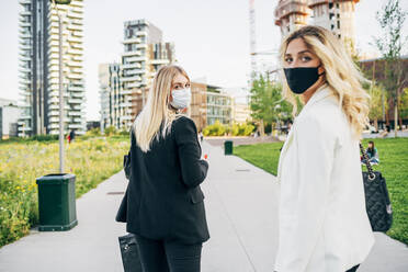Female coworkers wearing masks standing on footpath in city - MEUF01103