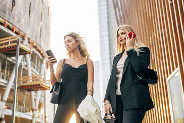 Weibliche Kollegen benutzen Smartphones, während sie an Gebäuden in der Stadt stehen - MEUF01108