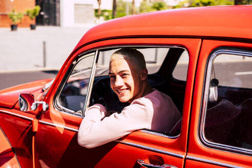 Porträt eines glücklichen Teenagers, der in einem Oldtimer sitzt und aus dem Fenster schaut - SIPF02172