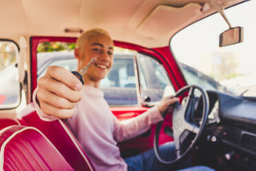 Happy teenage boy sitting in vintage car showing key - SIPF02173