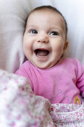 Portrait of happy baby girl in pink pyjama lying on bed - GEMF03890