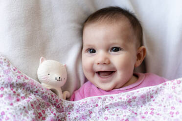 Portrait of happy baby girl lying on bed with teether - GEMF03891