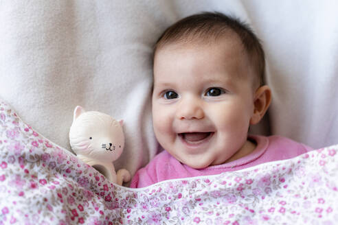 Porträt eines glücklichen kleinen Mädchens auf dem Bett liegend mit Beißring - GEMF03891