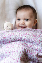 Portrait of happy baby girl lying on bed with teether - GEMF03892