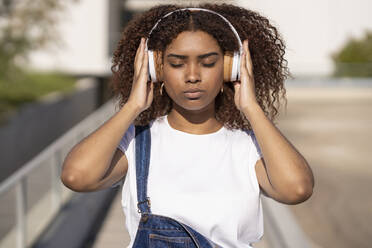 Nahaufnahme einer jungen Afroamerikanerin, die in der Stadt stehend Musik über Kopfhörer hört - JSMF01574