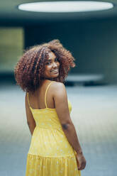 Lächelnde junge Frau in gelbem Kleid, die in einem Haus steht - JSMF01575