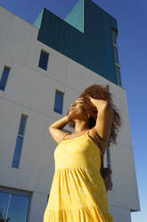 Carefree young woman with hands in hair standing against building - JSMF01586