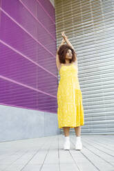 Nachdenkliche afroamerikanische Frau mit erhobenen Armen, die auf einem Fußweg gegen eine Mauer in der Stadt steht - JSMF01592