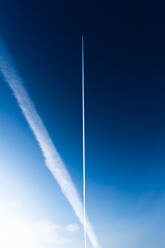 Chem trails from an airplane cross across a blue sky - CAVF86581