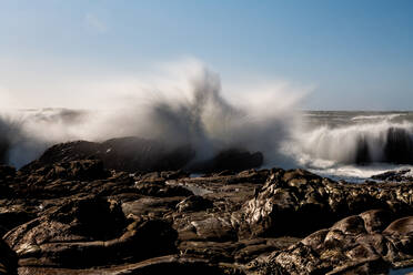 Long exposure of waves crashing over coastal rocks under blue sky - CAVF86589