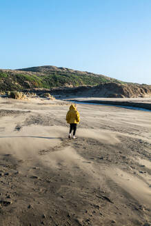 Boy walks on sandy beach tword fresh water stream leading to ocean - CAVF86594