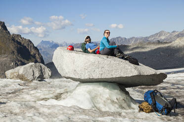 Couple sits on rock, Snowbird Glacier, Talkeetna Mountains, Alaska - CAVF86631